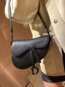 Model holding a black ultra-matte calfskin Saddle Bag over the shoulder