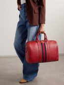Model carrying a Gucc! red textured Dollar calfskin large duffle bag with web stripe