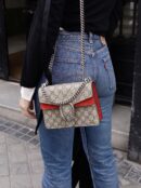 Model carrying a red GG Supreme monogram Small Dionysus shoulder bag with chain shoulder strap