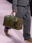 Model carrying an olive green grained calfskin Lingot 50 travel bag with detachable shoulder strap