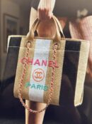 Model carrying a supeclone Ch@nel striped raffia and calfskin leather Deauville tote with multicolor logo