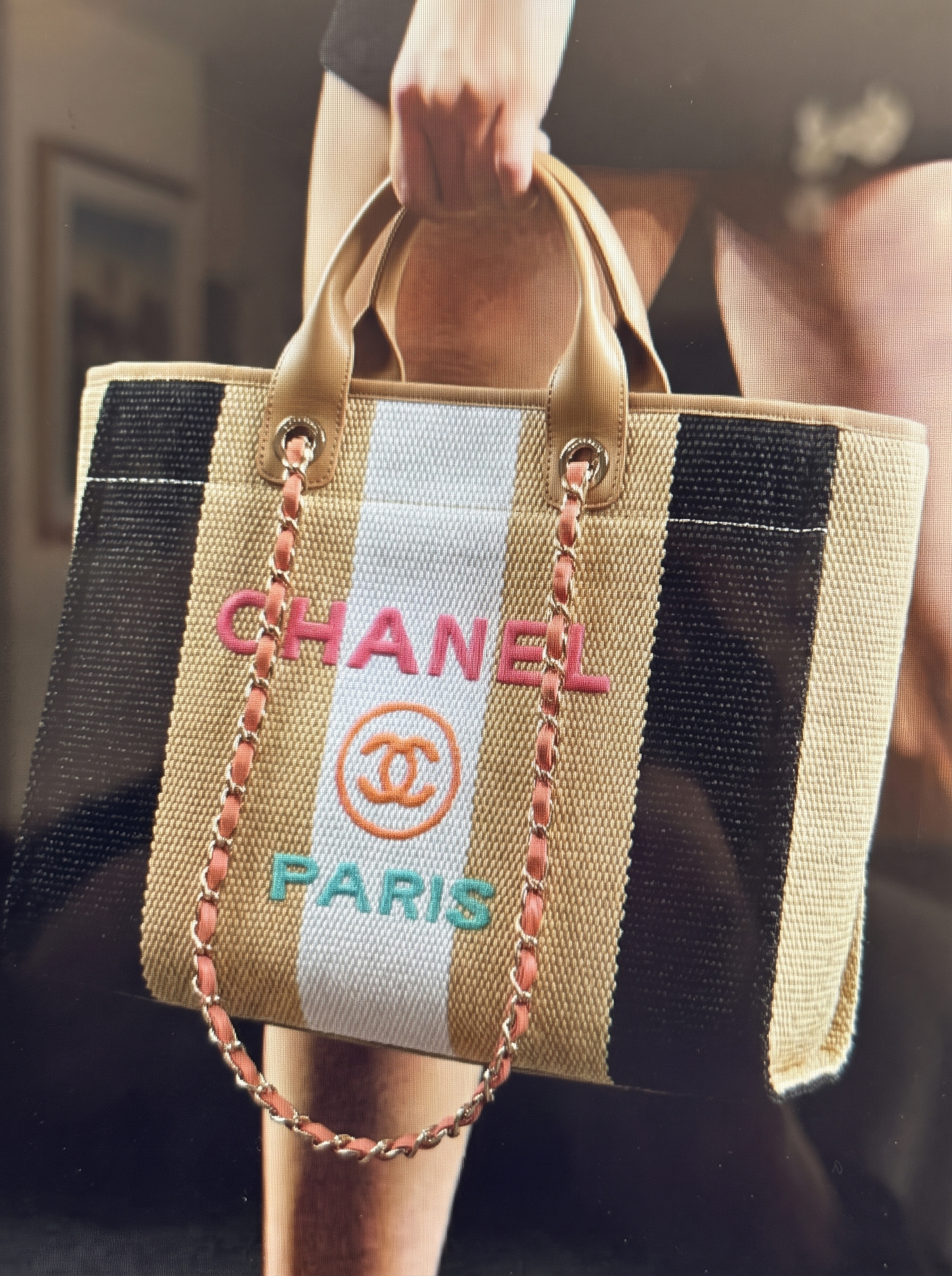 Model carrying a supeclone Ch@nel striped raffia and calfskin leather Deauville tote with multicolor logo