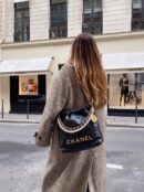 Model carrying the black crumpled calfskin Ch@nel Pearl Mini 22 bag with pearl detailing and chain shoulder strap