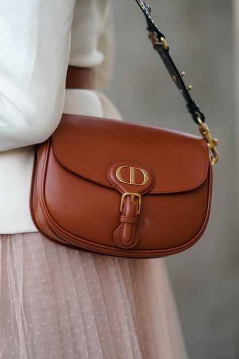 Model carrying the camel box calfskin D!0r Medium Bobby Flap Bag with adjustable leather shoulder strap