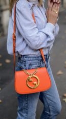 Model carrying the Gucc! Roxy Calfskin Blondie Chain Shoulder Flap Bag in Deep Orange